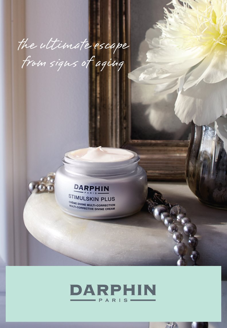 Open jar of Darphin StimuSkin Plus divine multi-corrective cream on a marble surface with white flowers, pearls, and a mirror background.
