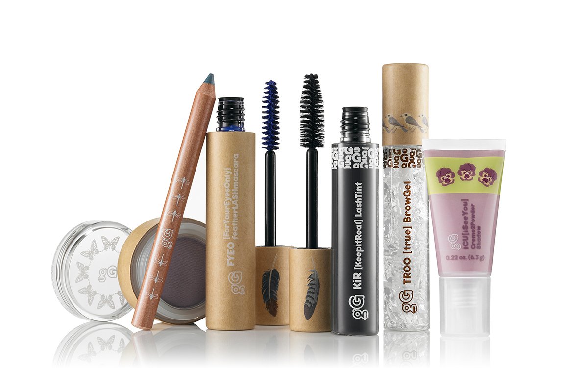 Collection of natural-colored makeup and cosmetic products including lipstick, mascara, brow gel, and lip gloss, with a butterfly design on one container and a purple flower design on another.